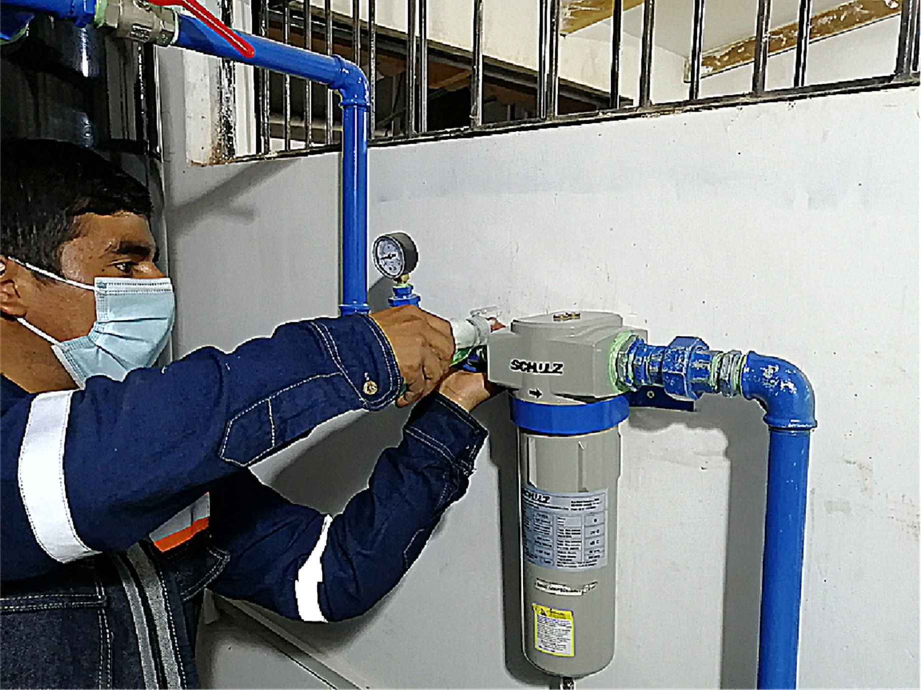 Técnico con mascarilla instalando un filtro en una tubería azul