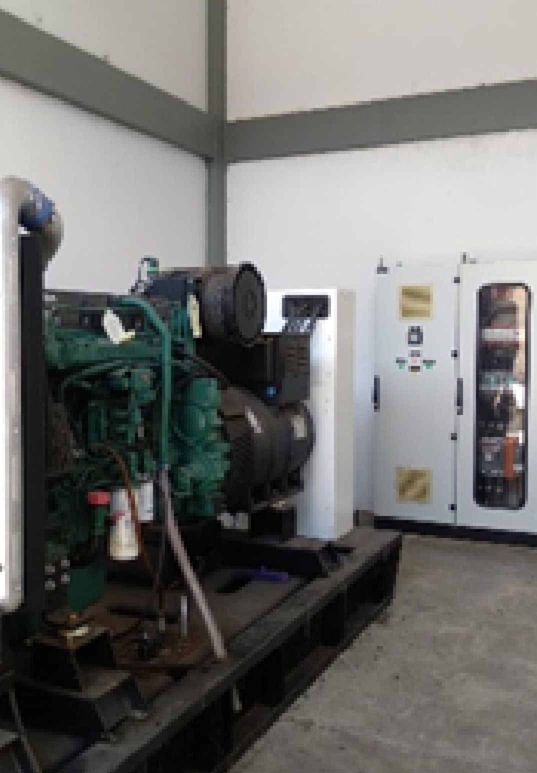 Grupo electrógeno con motor verde en una sala, junto a un gabinete blanco