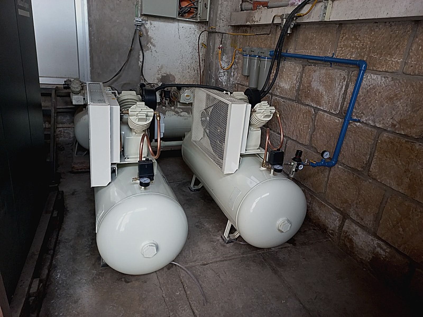 Dos compresores con tanques horizontales blancos junto a una pared de ladrillo
